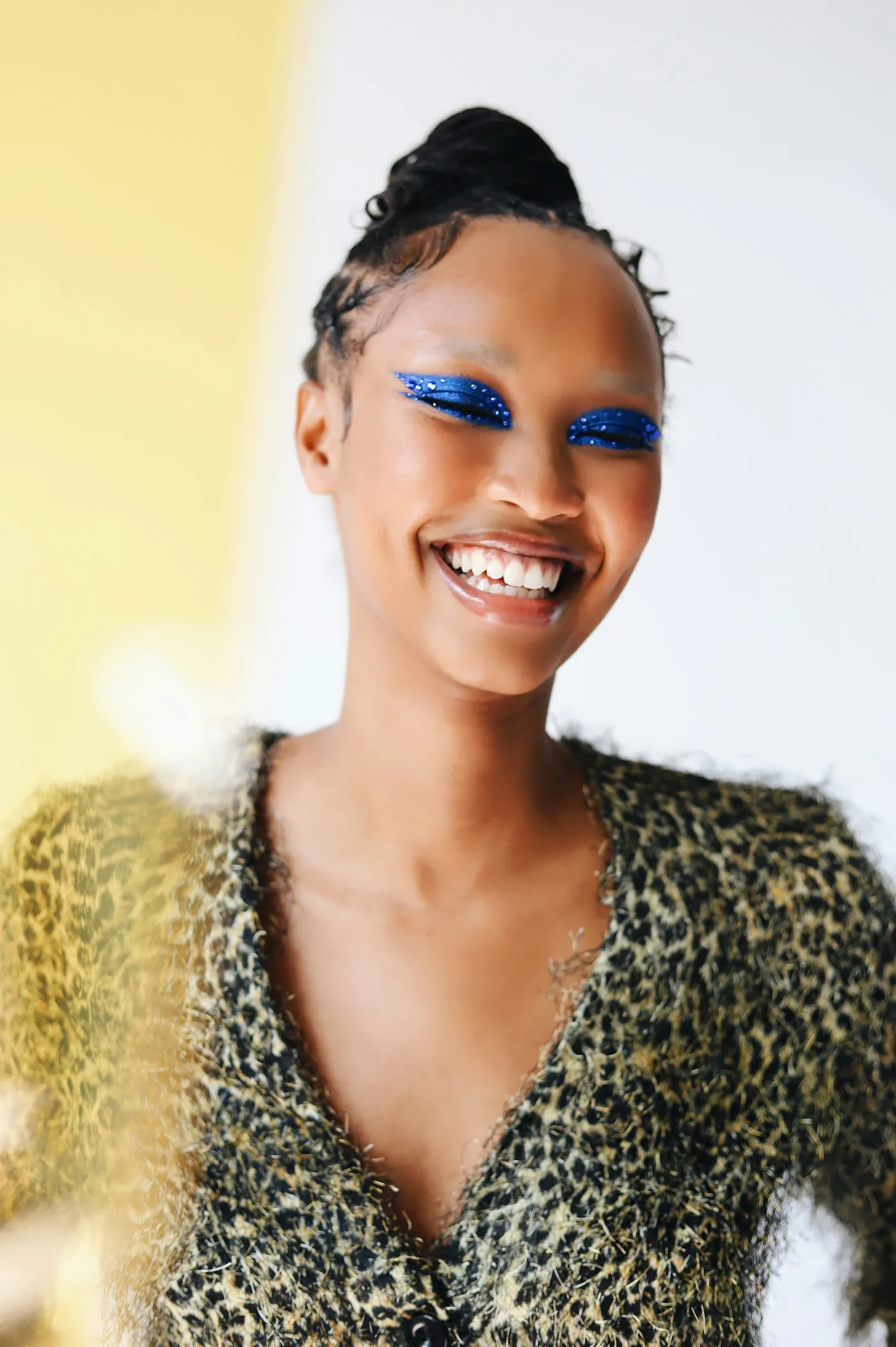 Une personne sourit, maquillage bleu pailleté sur les paupières.